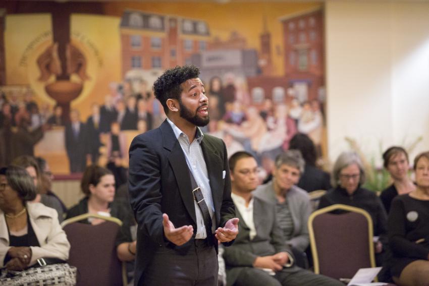 Amill stands and speaks in front of a crowd.