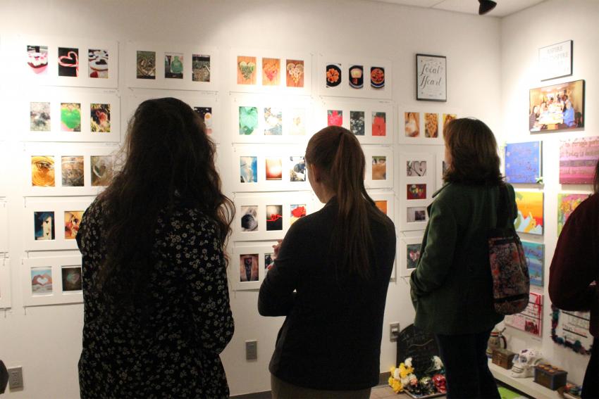 Three students face a wall filled with small photos in an art gallery