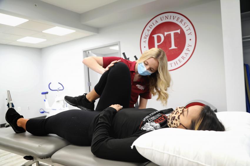 An Arcadia Physical Therapy student holds the knee of a female patient who is lying down