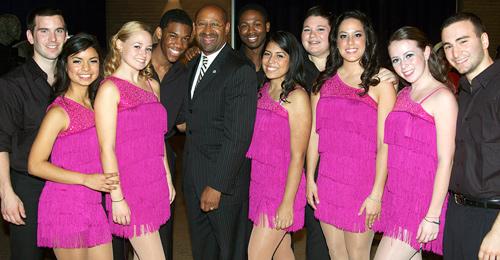 A group of people, with five women wearing pink dresses