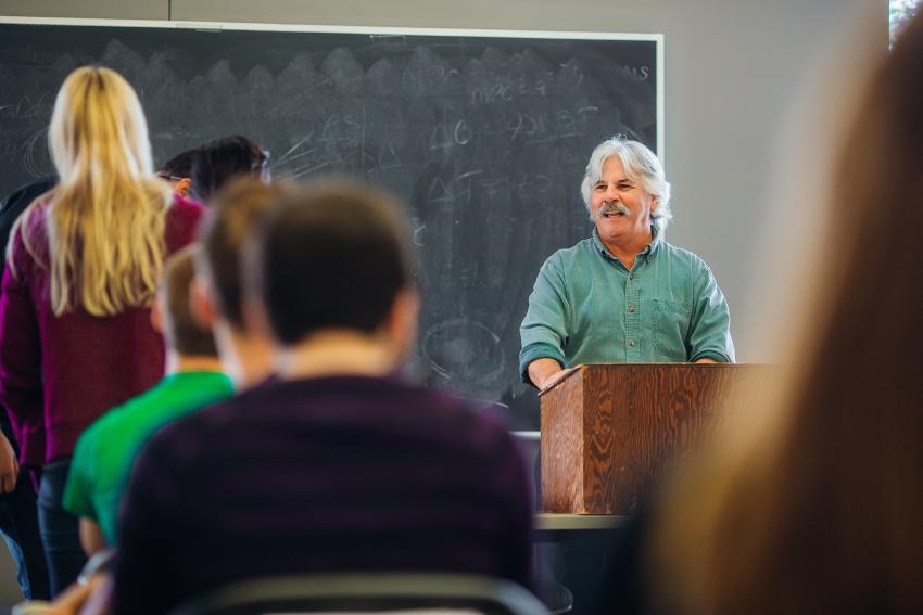 Dr. Morra smiles at a podium in front of his class.