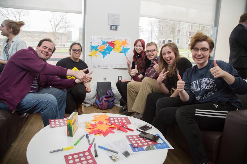 Transfer students gather on couches, smiling and holding thumbs-up