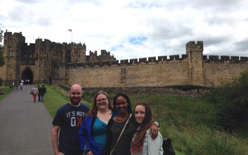 Four people standing together with a castle wall and entrance behind them