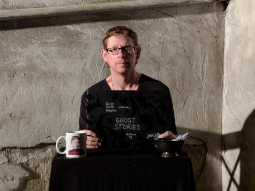 Person sitting at a table with a book titled "Ghost Stories", a coffee cup, and a bowl.
