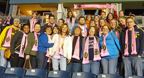 A group photo of students in the stands of a Philadelphia Union game wearing pink scarves