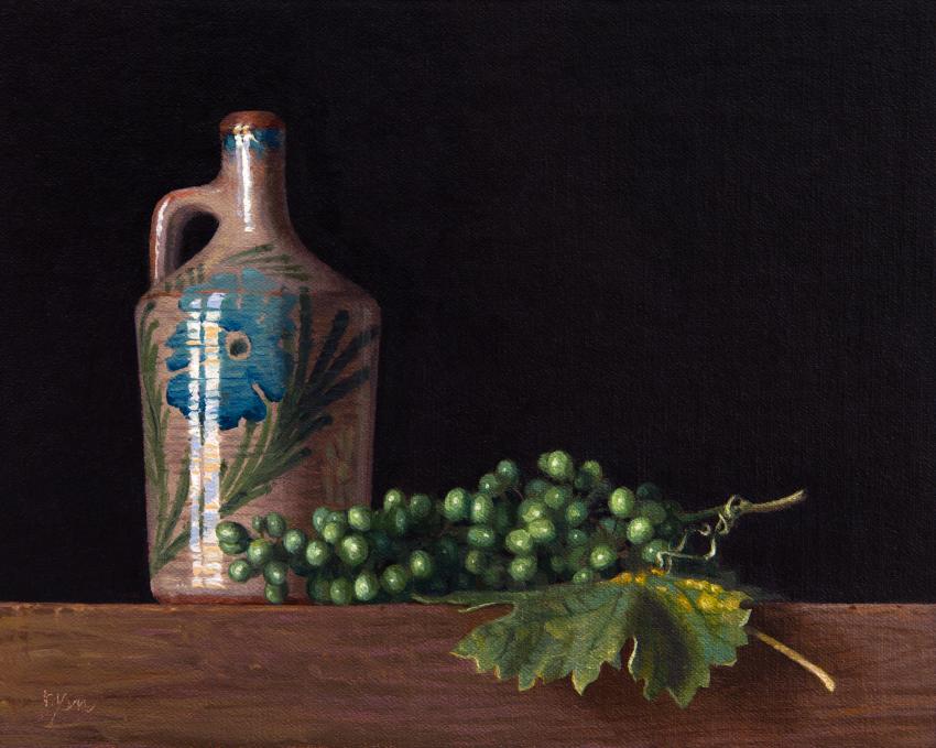 A ceramic floral jug next to a bunch of green grapes or olives