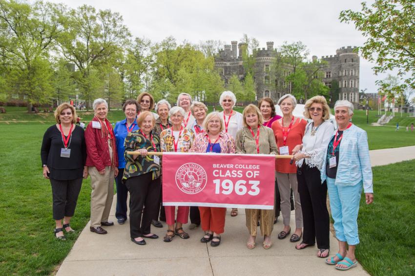 A group of a dozen and a half women stands on the Walk of Pride holding a Beaver College Class of 1963 banner