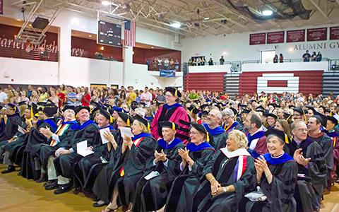 The Alumni Gym is filled with people in caps and gowns, applauding