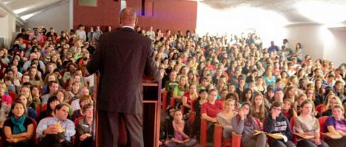 Man standing at a podium talking to a packed room of people
