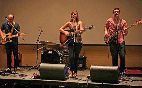 Three people on a stage playing guitars and singing.