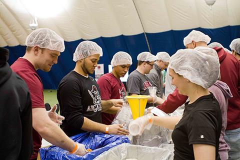 Wearing hairnets, Arcadia students volunteer gathered around a table scooping from large containers