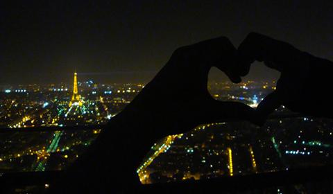 Someone making a heart shape with their hands with Paris in the background.