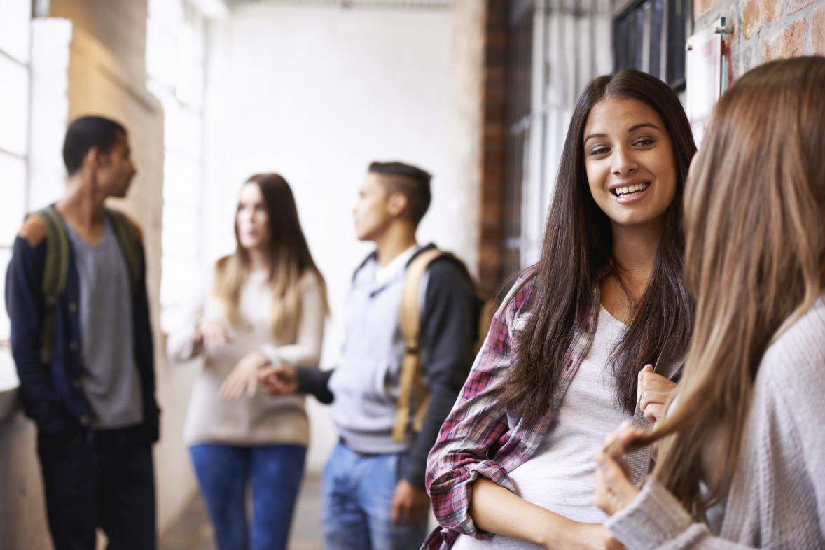 Groups of students talk outside a classroom.