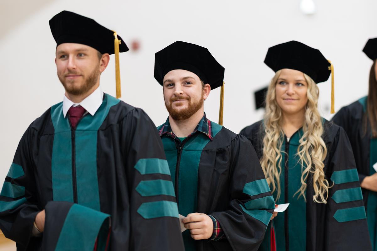 Three students walk into commencement wearing their graduation robes at DPT commencement on Oct. 29