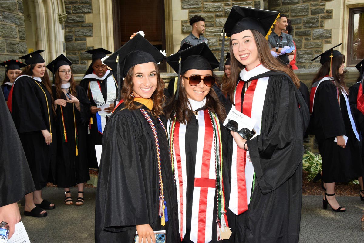 Three students smiling during the graduation ceremony on Haber Green 