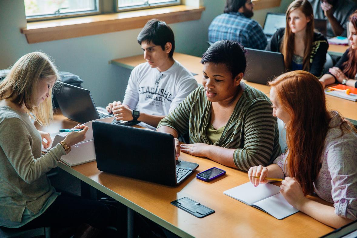 Lines of desks, students and laptops in a classroom