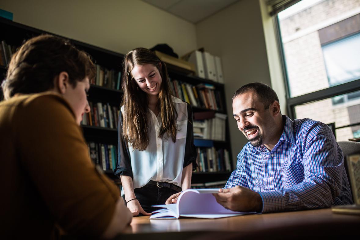 In a library two students talk to a faculty member.