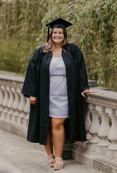 Catherine Bergmueller posing on a bridge and dressed in graduation attire