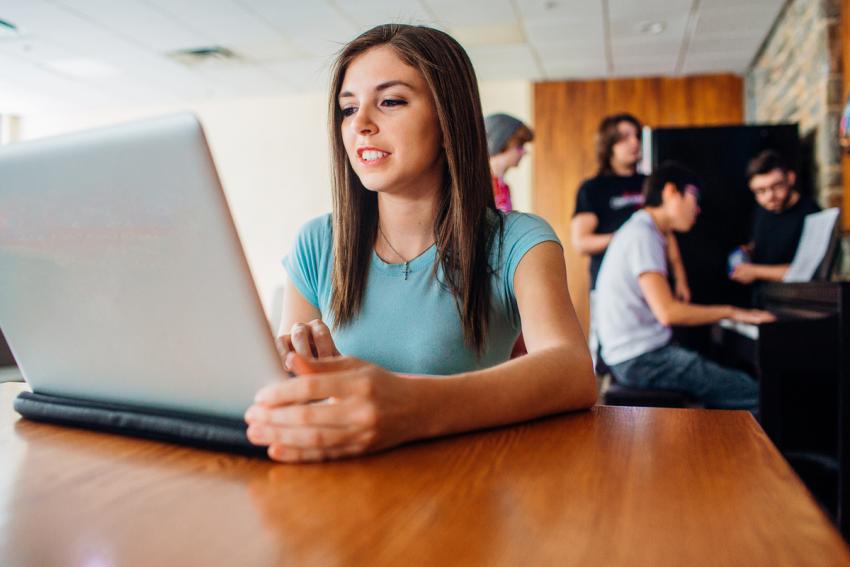 Person at table with laptop, others behind her around a piano