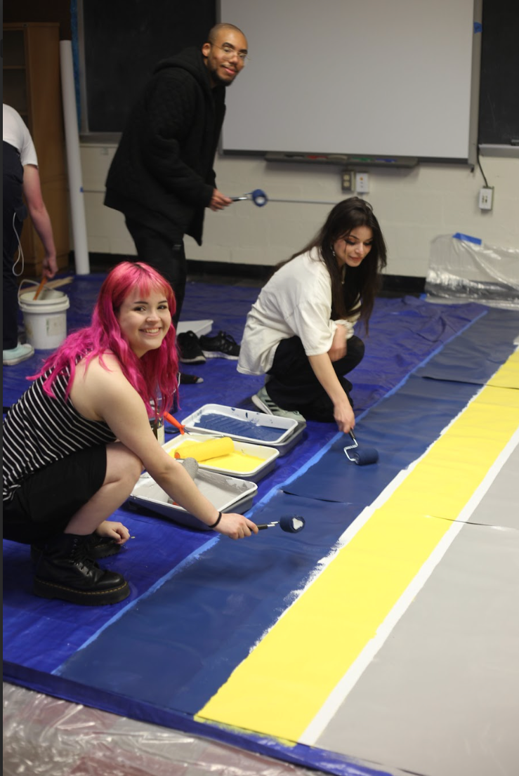 Students paint the Cheltenham mural using blue and yellow paint