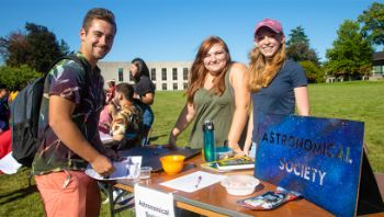 Astronomical Society student organization greeting a student at a table booth outdoors