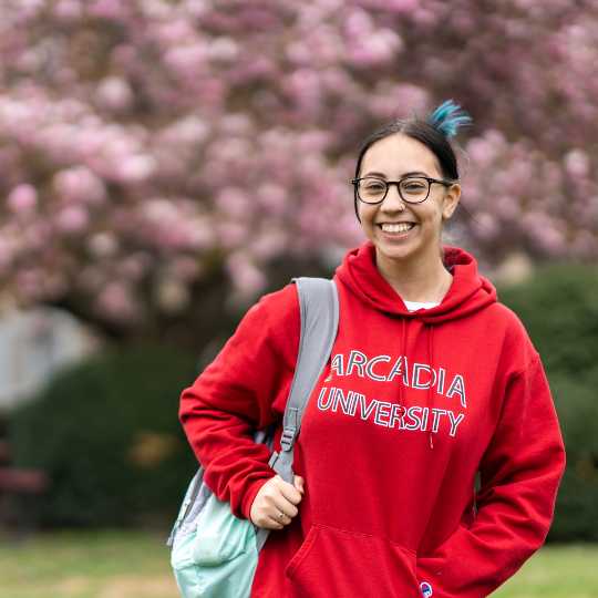 Smiling student with backpack wearing an Arcadia University hoodie sweatshirt from the campus store