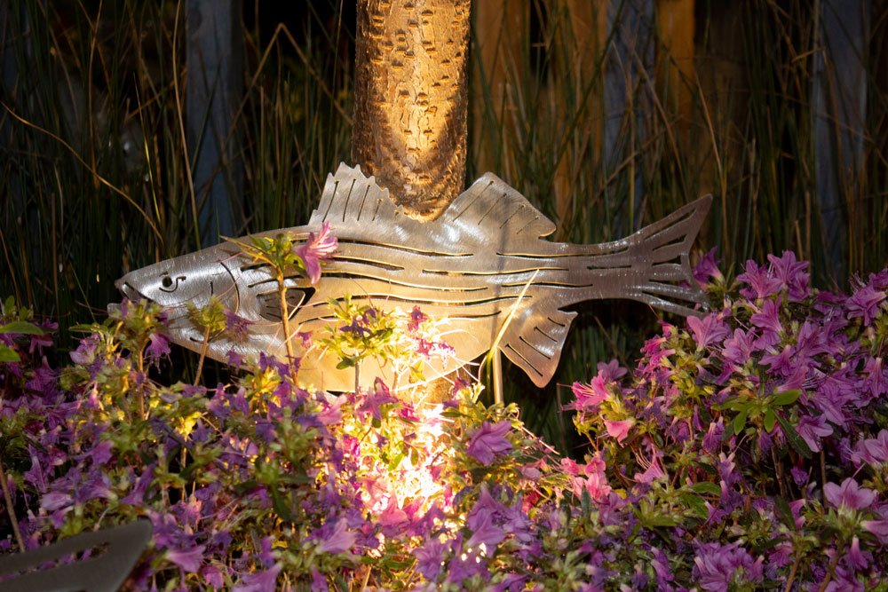 Metal fish sculpture with flower bouquets under it.