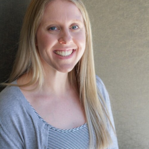 A headshot of a woman with long blonde hair wearing a grey cardigan over a striped shirt