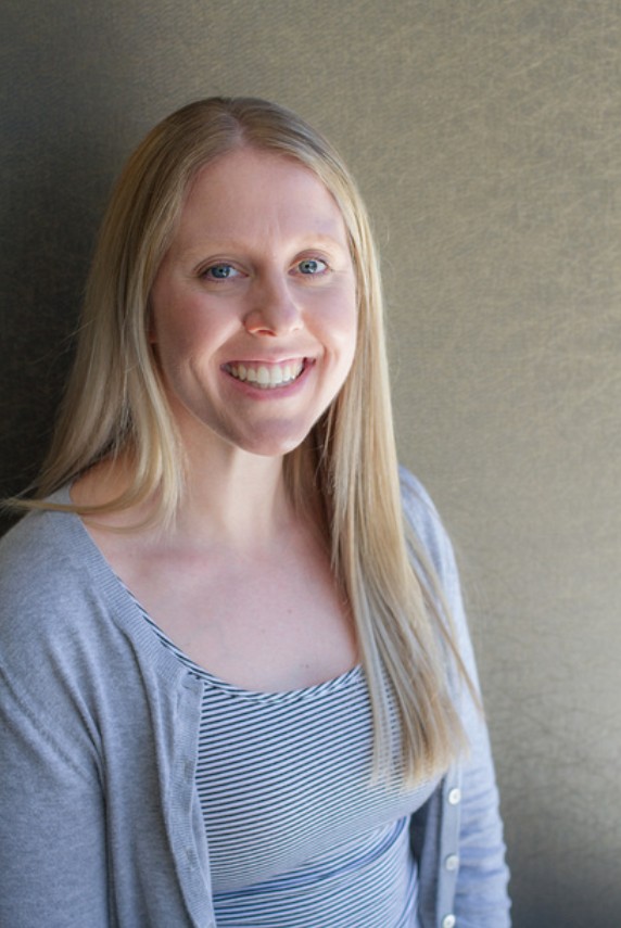 A headshot of a woman with long blonde hair wearing a grey cardigan over a striped shirt