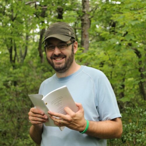 A portrait of a man in the woods holding a book