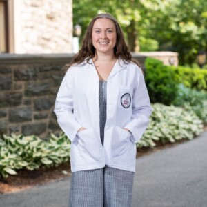 A photo of Martha Smee '25 MMS, MPH in a PA student white coat.