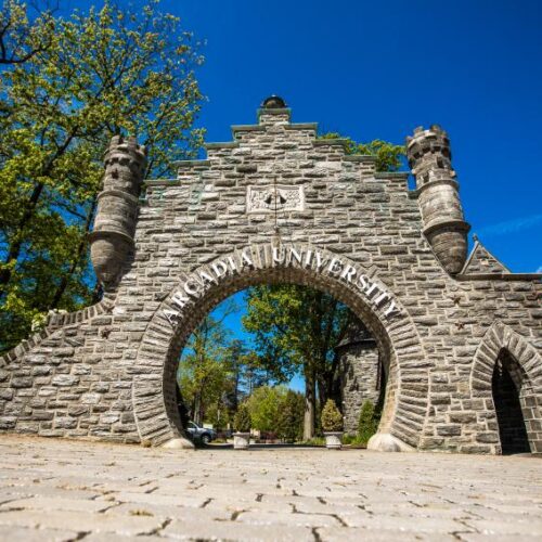 A large stone gate with a circular opening that reads "Arcadia University" over the arch of the opening
