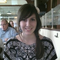 A square photo of a woman in a restaurant; another diner can be seen over her shoulder