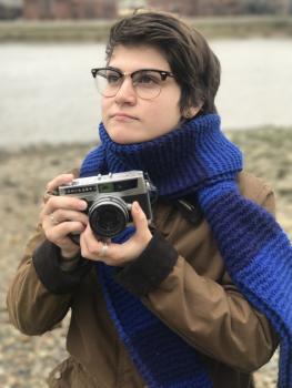 Person holding a camera and wearing a blue scarf and brown jacket