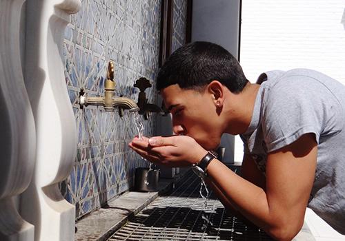 Young man leaning over a faucet to drink water.