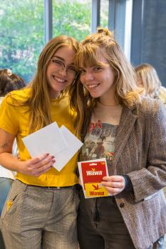 Two young women smile at the camera, their faces close together, holding a Wawa gift card and two white envelopes