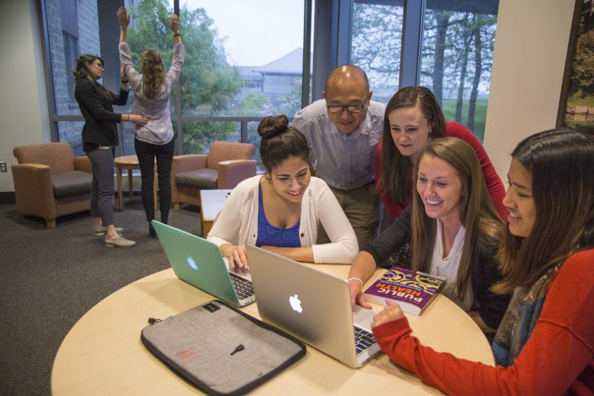 Arcadia students study around a table and look at computer screens indoors.