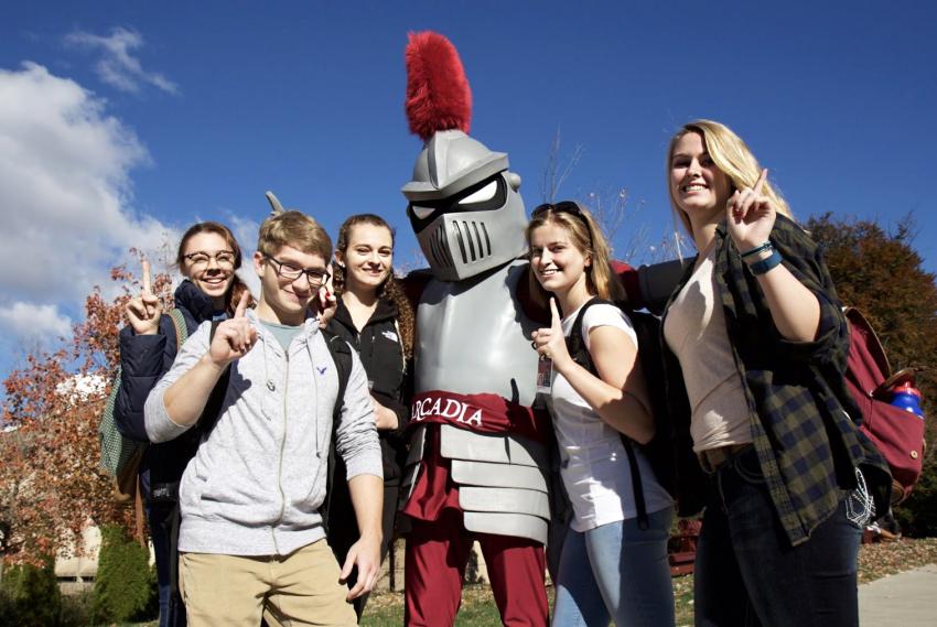 Five students and Archie the Knight mascot all hold up one finger