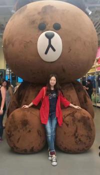 Victoria Wang stands in front of a giant brown stuffed bear