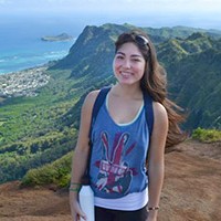 Airi S. standing cliffside of the ocean.