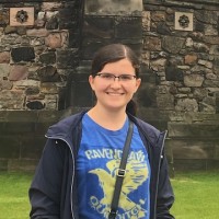 A student smiles in front of a stone wall or structure