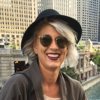 A portrait of Lauren Young / a woman wearing a black hat with buildings in the background