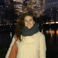 Amelia Graf in a coat and scarf in front of a pond and tall buildings.