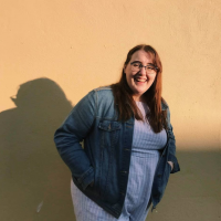 A young woman with long brown hair smiles at the camera. Her face is in the sun, while her body is in the shade.