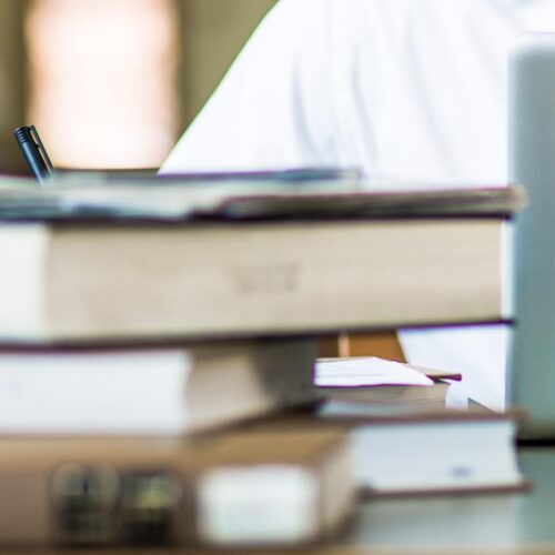 Books and laptop in front of a person working.