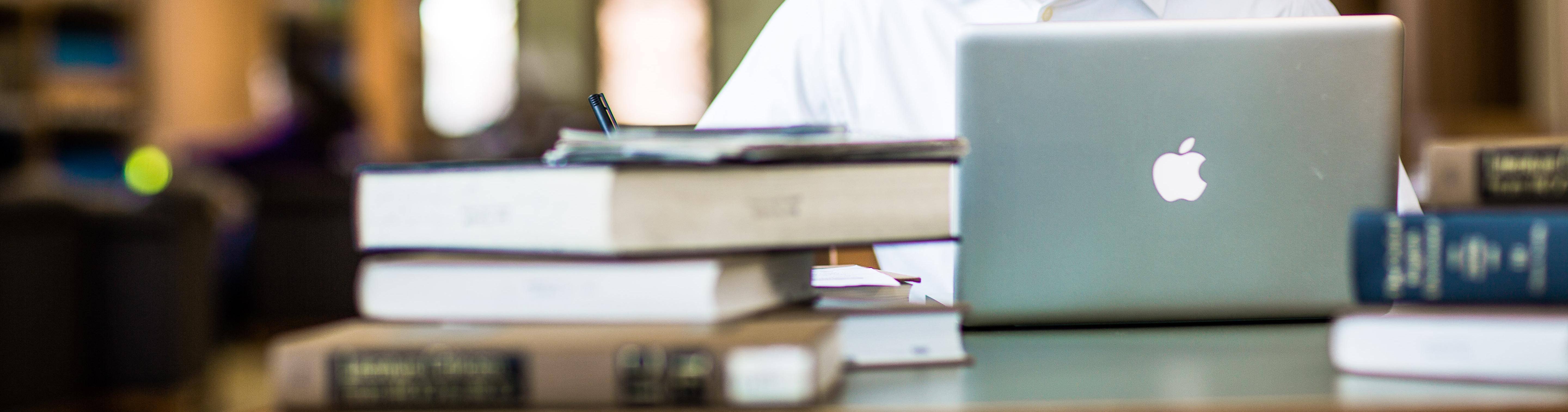 Books and laptop in front of a person working.