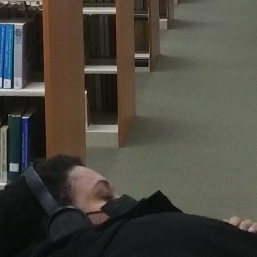 Student relaxing in library holding a book with eyes closed and headphone on
