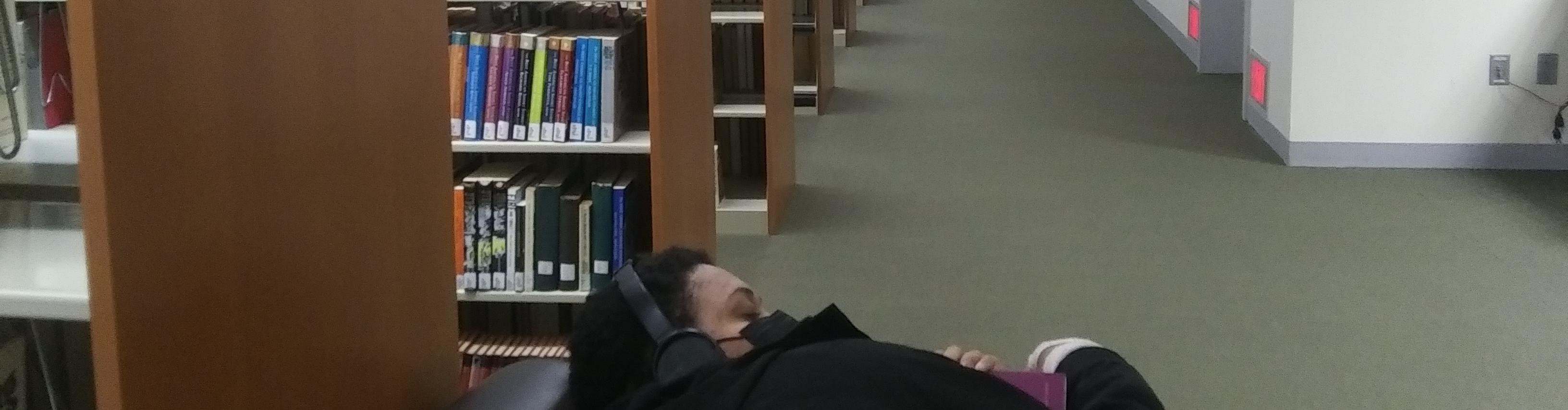 Student relaxing in library holding a book with eyes closed and headphone on