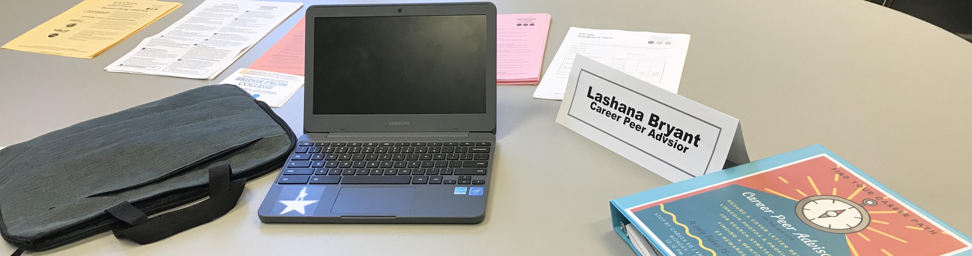 A desk area with a laptop, career prep papers, and name tag of Lashana Bryant, Career Peer Advisor
