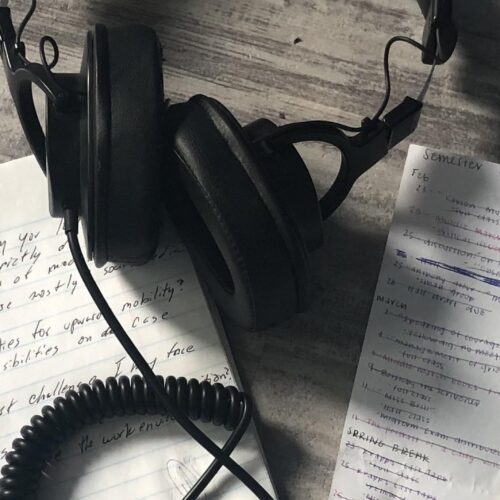 A pair of headphones and note paper on a gray wooden table.